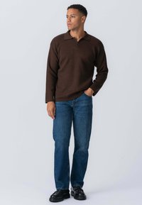 Brun strikket polo sweater med lange ærmer, parret med blå lige ben jeans og sorte sko med kraftig sål. Enkel, klassisk design.