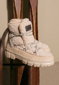 Stivaletti beige alla caviglia con texture soffice, dotati di colletto imbottito, stringhe grigie e suola spessa. Etichetta con accento in pelle sul lato.