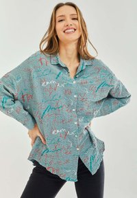 Light blue button-up shirt with an oversized fit, featuring a textured surface and colorful handwritten patterns in red, turquoise, and white.