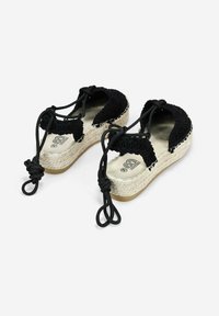 Espadrillas de ganchillo negras con suela de paja trenzada. Cuenta con cordones negros ajustables y una suela de goma plana. Diseño superior texturizado.
