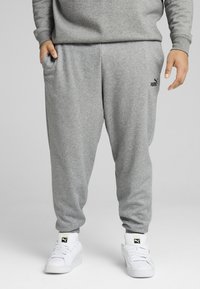 Grå bomulds sweatpants med elastisk talje, sidelommer og lille sort Puma-logo på venstre lår. Parret med hvide sneakers.