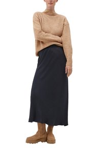 Béžový pletený svetr s vysokým límcem, tmavě modrá midi sukně a hnědé kotníkové boty. Ležérní outfit s jemnými texturami a pohodlným střihem.