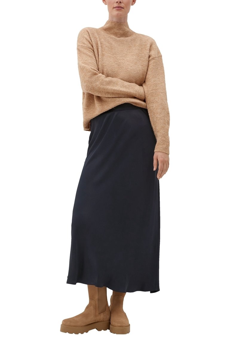 Béžový pletený svetr s vysokým límcem, tmavě modrá midi sukně a hnědé kotníkové boty. Ležérní outfit s jemnými texturami a pohodlným střihem.