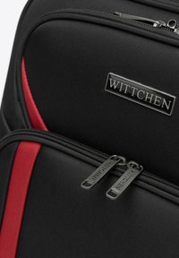 Černý tkaninový batoh s červenými akcenty, který má dva zipové oddíly a metalickou logo destičku. Texturovaný povrch pro zvýšenou odolnost.