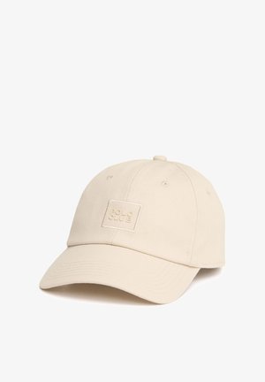 Cappellino da baseball beige con visiera curva e piccola toppa quadrata sul davanti con scritta "POLA CAVE" in rilievo.