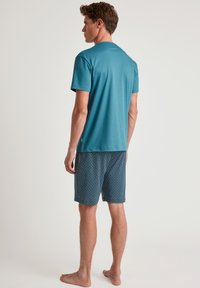 Teal T-shirt met korte mouwen, gecombineerd met gestreepte marineblauwe shorts met kleine ronde patronen. Katoenmengsel, relaxte pasvorm.