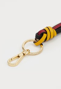 Attache clé en cuir avec des sangles noires, bordeaux et jaunes entrelacées, équipé d'un clip en métal doré et d'un anneau circulaire.