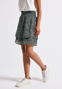 Green and white patterned skirt with a layered design, featuring a stretchy waistband and hem above the knee, paired with white sneakers.