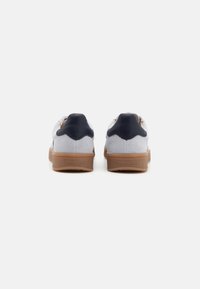 Paire de baskets en suede gris clair avec des languettes de talon noires et des semelles en caoutchouc couleur gomme vues de dos sur un fond blanc.