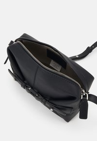 Borsa a tracolla nera in pelle con chiusura a zip, caratterizzata da una superficie morbida e textured e un dettaglio a fiocco sul davanti. Etichetta interna visibile.