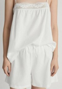 Outfit casual alb format dintr-un top fără mâneci, lejer, cu dantelă și șorturi cu talie elastică și șnur. Textură moale.