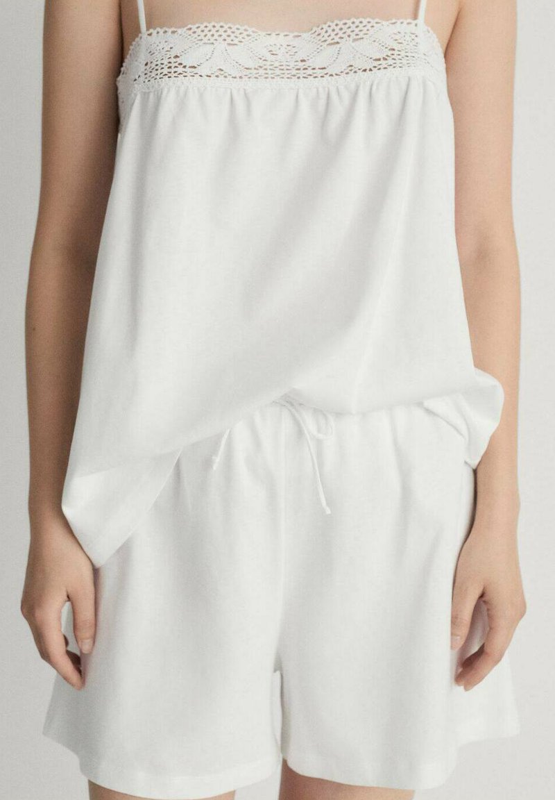 Outfit casual alb format dintr-un top fără mâneci, lejer, cu dantelă și șorturi cu talie elastică și șnur. Textură moale.