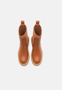 Bottes de cheville brunes avec un extérieur en cuir lisse, des panneaux latéraux élastiques et un tissu texturé sur le dessus. Semelles rembourrées pour plus de confort.
