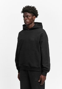 Black hoodie made of cotton blend, featuring a front pocket, drawstring hood, and minimalistic logo on the chest. Soft, smooth texture.