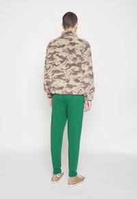 Fleece jacket in beige with brown camouflage pattern, paired with green sweatpants. Includes a stand collar and elastic cuffs.