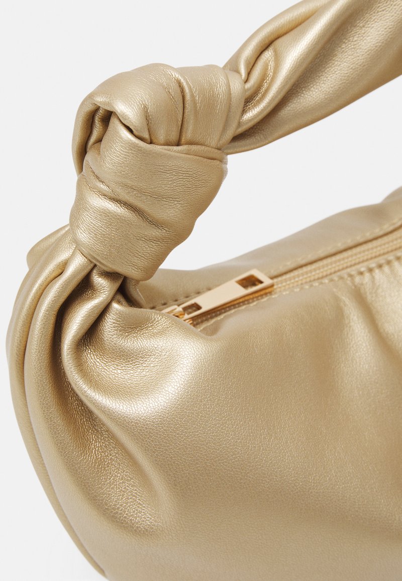 Bolso de mano de cuero texturizado dorado con un asa anudada y cierre de cremallera. Presenta un acabado suave y detalles en dorado.