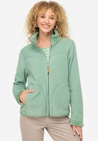 Veste en polaire vert clair avec un col haut, fermeture éclair et deux poches avant. Texture douce et les poignets présentent un bord contrastant.