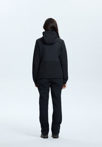 Veste noire isolée avec capuche, présentant une texture lisse et un design ajusté, associée à un pantalon noir assorti et des chaussures robustes.