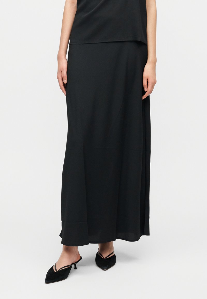 Μαύρη, αέρινη μακρυμάνικη φούστα από λείο υλικό, με ίσια κοπή, ελαφρώς στρωματοποιημένο πάνω μέρος και πλευρική σχισμή.