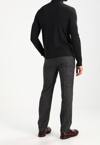 Tmavě šedý vlněný svetr s vysokým límcem, kombinovaný se světlými šedými vlněnými kalhotami s texturou. Outfit doplňují hnědé kožené boty.