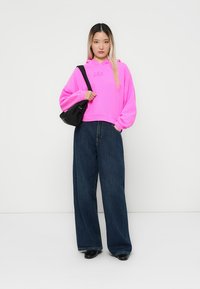 Rosa sweatshirt med "GAP"-logo, oversized passform, kombinert med vide mørke denimjeans. svart crossbody-veske gir kontrast. Flate sko.