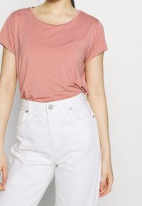 T-shirt rosa a maniche corte con scollo rotondo, abbinato a jeans bianchi a vita alta con chiusura a bottoni e tasche laterali.