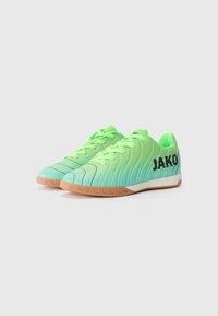 Groene gradient sport schoenen met een geribbelde bovenkant, zwarte "JAKO" branding en een lichtbruine rubberen zool. Veters zijn ook groen.