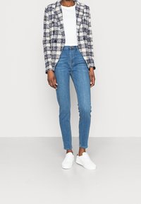 Kostkovaný blejzr v námořnické modři a krémové barvě s dvouřadým zapínáním, kombinovaný s vysokými modrými skinny džínami a bílými teniskami.