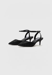 Escarpins noirs à talon slingback avec un bout pointu et une surface texturée pailletée, dotés d'une fine bride à la cheville et d'un talon petit d'environ 5 cm.