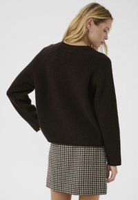 Brun stickad tröja med ribbat mönster, avslappnad passform och långa ärmar, tillsammans med en rutad kjol i beige, bruna och blå nyanser.