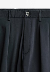 Svarta byxor med slät fronts, med två veck, knappstängning och sidofickor. Tillverkade av ett glatt, hållbart tyg.