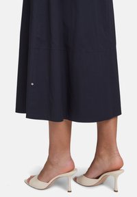 Robe midi navy avec une silhouette droite, ornée d'un accent argenté près de l'ourlet. Associée à des sandales ouvertes beige.