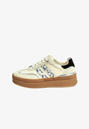 White sneaker with suede and leather materials, featuring grey leopard print accents, a thick brown sole, and metallic detailing.