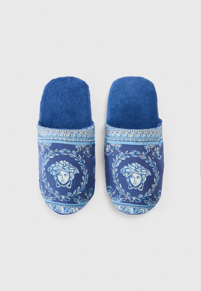 Blaue Hausschuhe mit einer strukturierten Oberfläche und einem aufgedruckten Design mit Gesichtern und Lorbeer-Motiven; weicher Stoff und kontrastierende blaue Akzente.