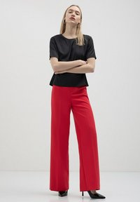 Top nero a maniche corte abbinato a pantaloni a gamba larga rossi a vita alta e décolleté nere a punta. Tessuto liscio, silhouette moderna.