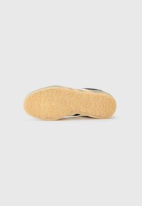 De zool van een sneaker heeft een gemusterde rubberen oppervlakte met cirkelvormige ontwerpen, tegen een effen witte achtergrond.
