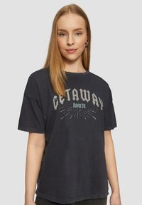 Zwarte grafische t-shirt met korte mouwen, met de tekst "GETAWAY ROUTE" in blokletters en radiale lijnen, zachte katoenen textuur.