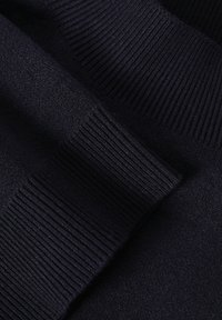 Le tissu en maille bleu marine présente une texture lisse avec des détails côtelés le long des bords, créant un effet superposé.