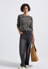 Haut en tricot à manches longues noir et beige rayé zèbre, associé à un jean large taille haute gris foncé et un sac à épaule en daim beige.