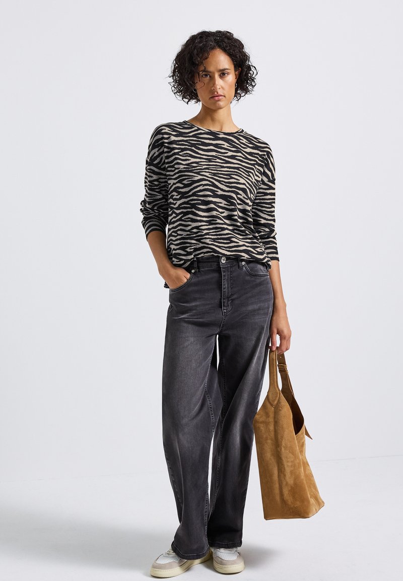 Haut en tricot à manches longues noir et beige rayé zèbre, associé à un jean large taille haute gris foncé et un sac à épaule en daim beige.