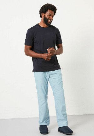 Navy cotton t-shirt, light blue striped pants with a relaxed fit, and navy slip-on shoes. Subject stands casually with hands clasped.