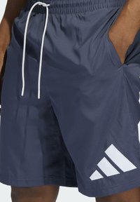 Marinblå idrottsshorts i ett lätt material, med en vit dragsko och en framträdande vit tre-stripes-design på vänster ben.