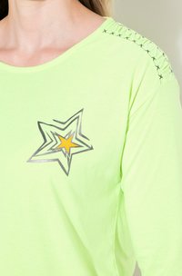 Hellgrünes Langarmshirt mit einem Sternenmotiv in Schwarz und Gelb. Verfügt über geraffte Nähte am Halsausschnitt. Glattes, lässiges Material.