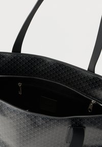 Μαύρη τσάντα tote με γεωμετρικό ανάγλυφο σχέδιο, λείο υλικό, εσωτερική τσέπη με φερμουάρ και διπλούς ιμάντες ώμου.