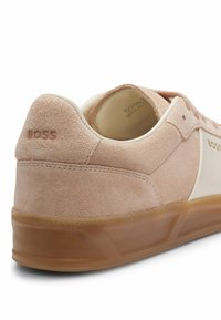 Μπεζ σουέντ αθλητικό παπούτσι με καουτσούκ σόλα, με ανάγλυφο «BOSS» στη φτέρνα και πλευρά, που δείχνει λεπτομέρειες από πίσω και πλευρικά σε λευκό φόντο.