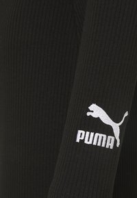 Vêtement à manches longues noir côtelé avec un logo Puma blanc brodé sur la manche droite. Le tissu a une texture lisse.