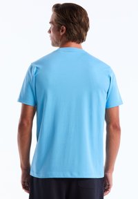 T-shirt à manches courtes en coton bleu clair avec un col rond. Texture lisse sans motifs ni accents visibles. Conçu pour une tenue décontractée.
