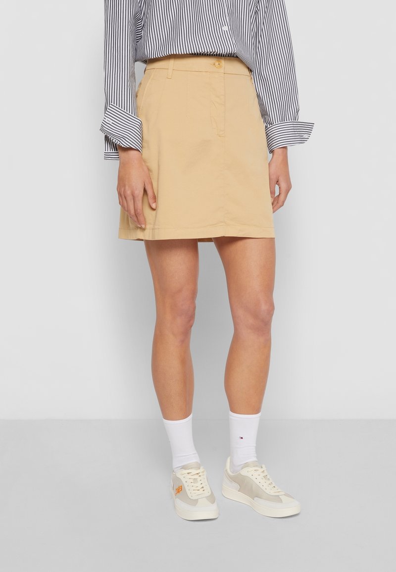 Beige bomullskjol med rak skärning, med knappstängning och sidofickor. Tillsammans med vita strumpor och beige sneakers.