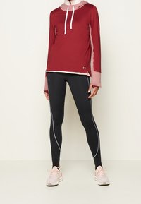Bordeauxfarbiges Sportoberteil mit Kapuze und langen Ärmeln, kombiniert mit schwarzen Leggings mit weißen Paspeln, ergänzt durch helle rosa Sneakers.