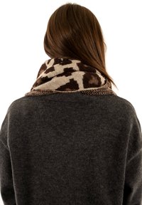 Écharpe en mélange de laine avec un imprimé léopard marron et crème, enroulée autour du cou, avec un pull en gris foncé texturé visible.
